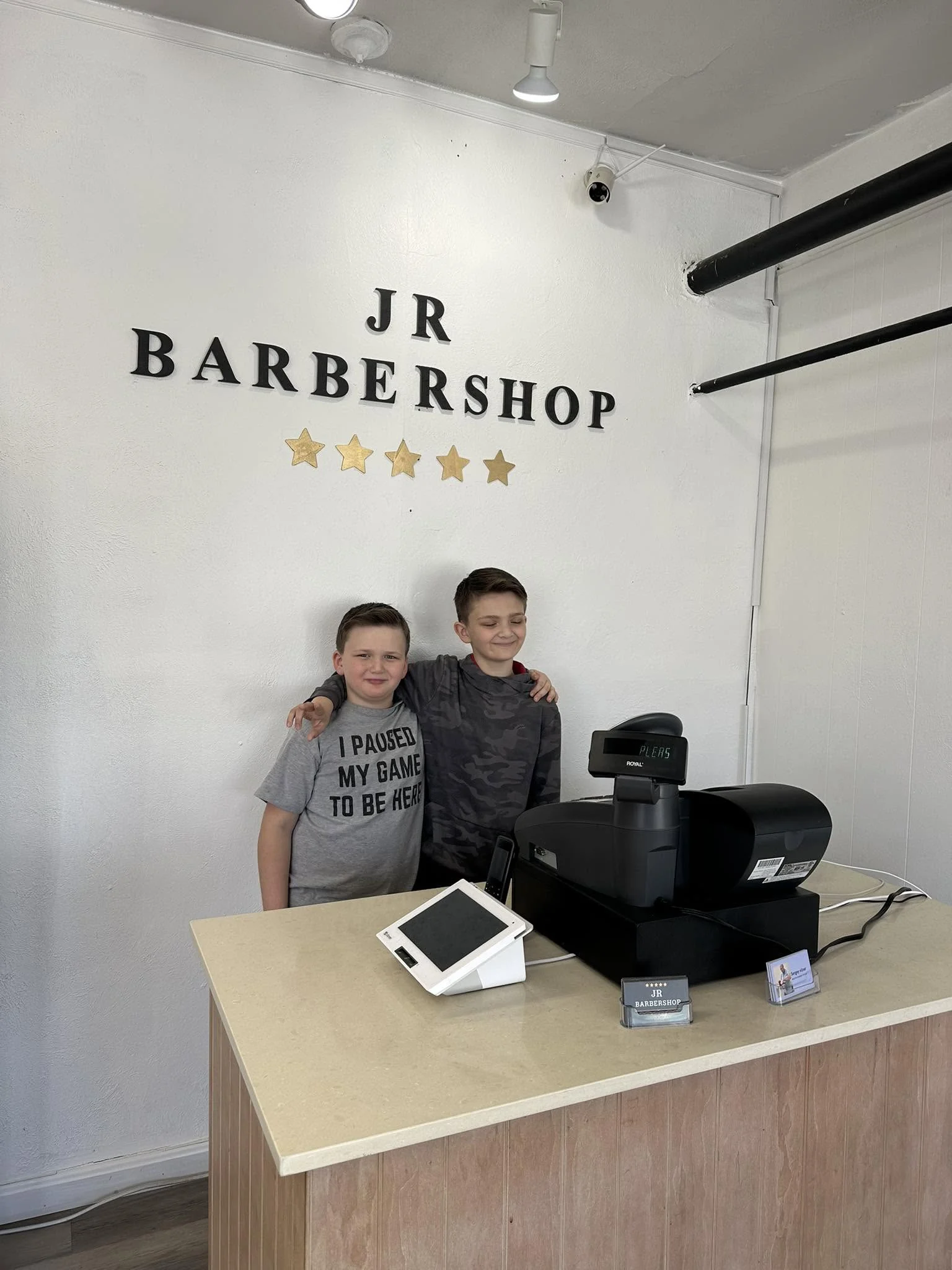 Two young visitors standing together behind the reception counter at JR Barbershop