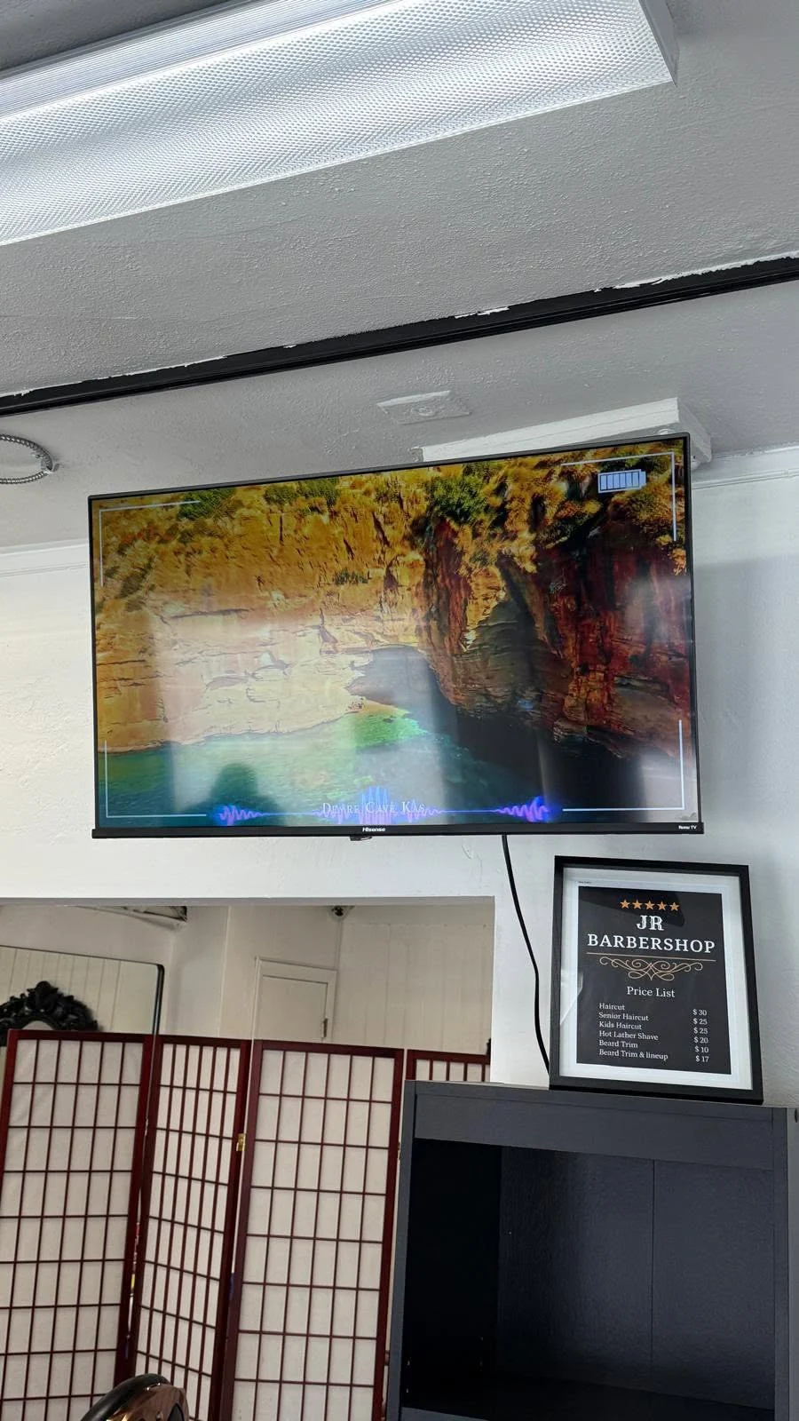 Television and framed shop artwork on the wall inside JR Barbershop