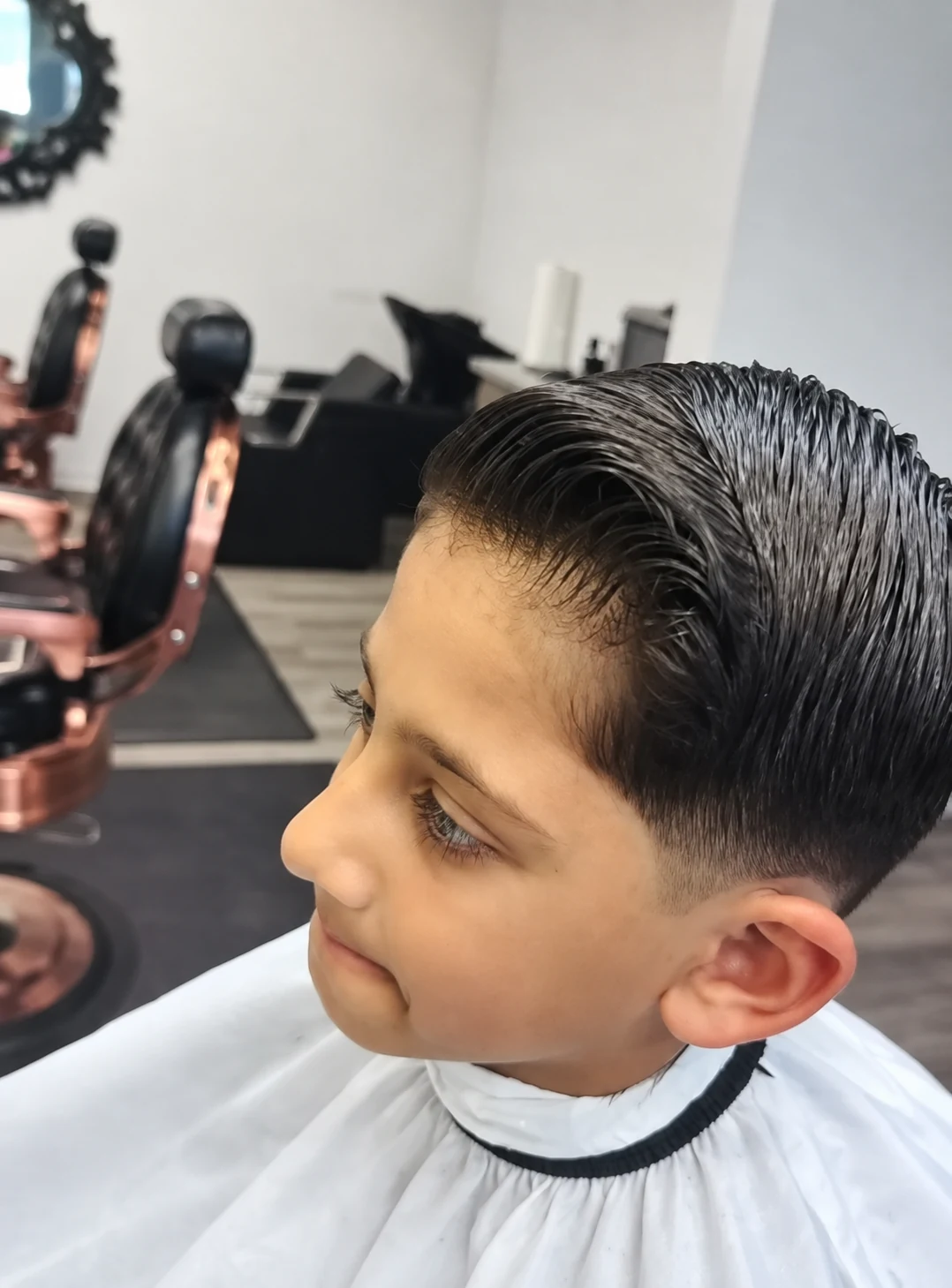 Side-part haircut with tapered sides on a client wearing a white barber cape at JR Barbershop